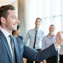 Cheerful leader motivating his business team. Handsome young politician telling his plan and showing fist as symbol of power. Positive business people standing in background. Strong company concept