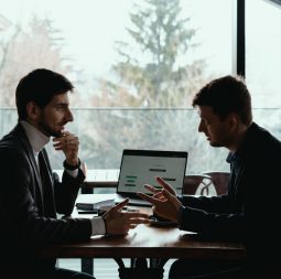 Two businessmen talking about new opportunities sitting with laptop at desk, planning project, considering business offer, sharing ideas while drinking coffee together