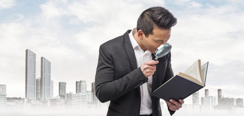 young asian business man looking through a magnifying glass