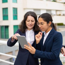 Content businesswomen using tablet pc. Cheerful focused female colleagues standing with digital tablet on urban city street. Wireless technology concept