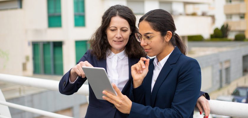 Content businesswomen using tablet pc. Cheerful focused female colleagues standing with digital tablet on urban city street. Wireless technology concept